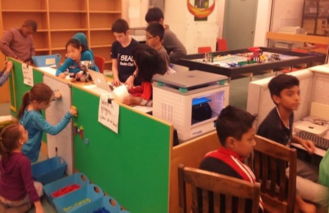 This is an image of a makerspace in a school with students around a 3D printer and working on a lego wall