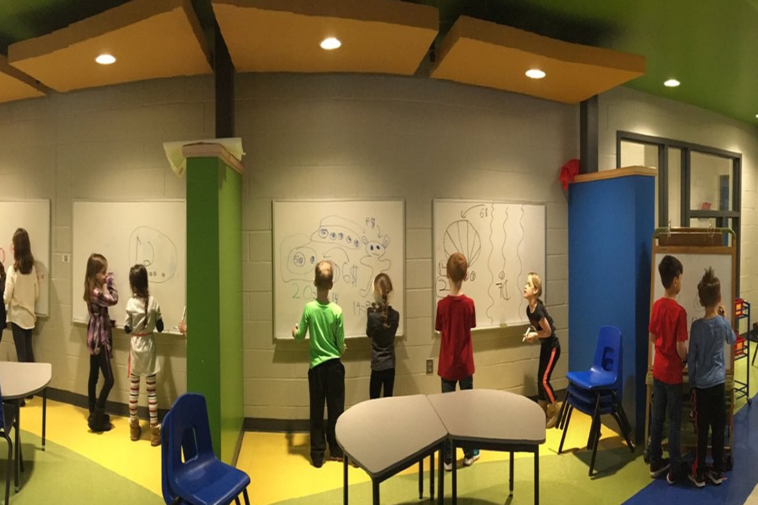 This is an image of students working together on whiteboards in the hall of a school.